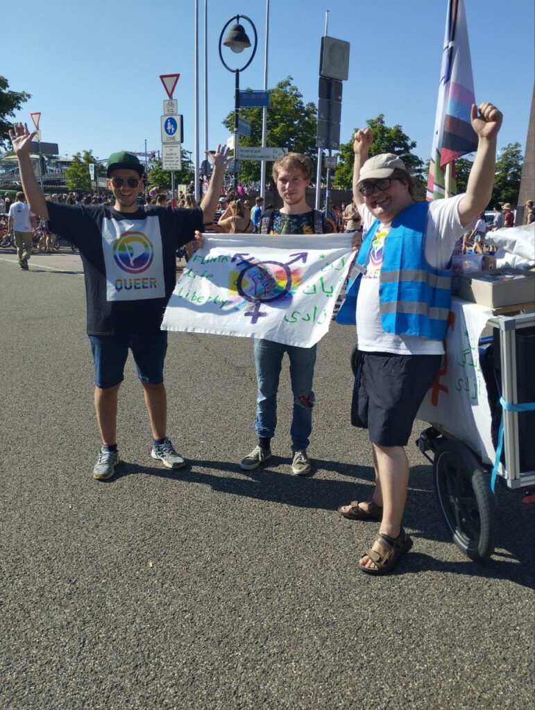 Drei Menschen mit einem queerpolitischen Banner nach dem CSD